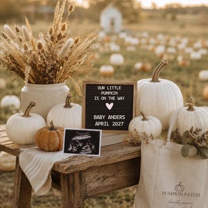 May include: A wooden letter board with the text OUR LITTLE PUMPKIN IS ON THE WAY, a heart icon, BABY ANDERS, and APRIL 2027. It sits on a wooden table with white and orange pumpkins, a dried floral arrangement, an ultrasound photo, and a tote bag.