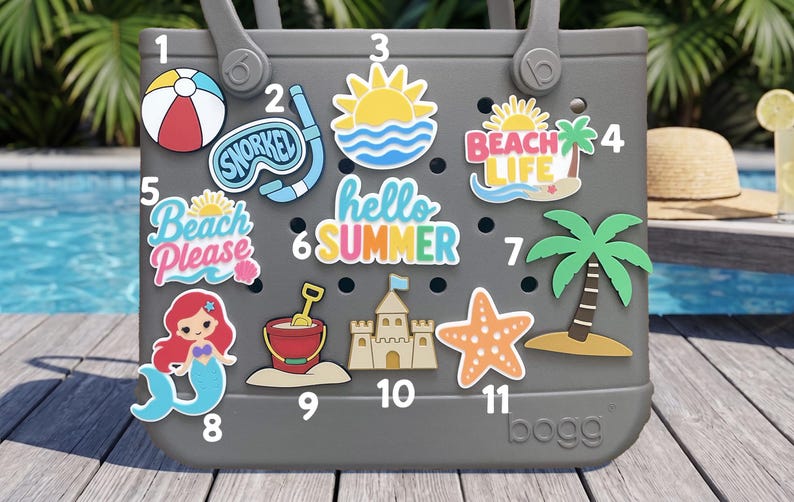 May include: A gray tote bag featuring eleven colorful summer-themed decorative inserts. The inserts include a beach ball, snorkel, sun, beach life text, beach please text, hello summer text, palm tree, mermaid, bucket, sandcastle, and starfish.