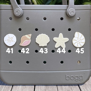 May include: A gray rubber tote bag featuring five circular holes across the front, each decorated with a different sea-themed charm labeled 41 through 45. The charms include a sand dollar, a conch shell, a scallop shell, a starfish, and a nautilus.