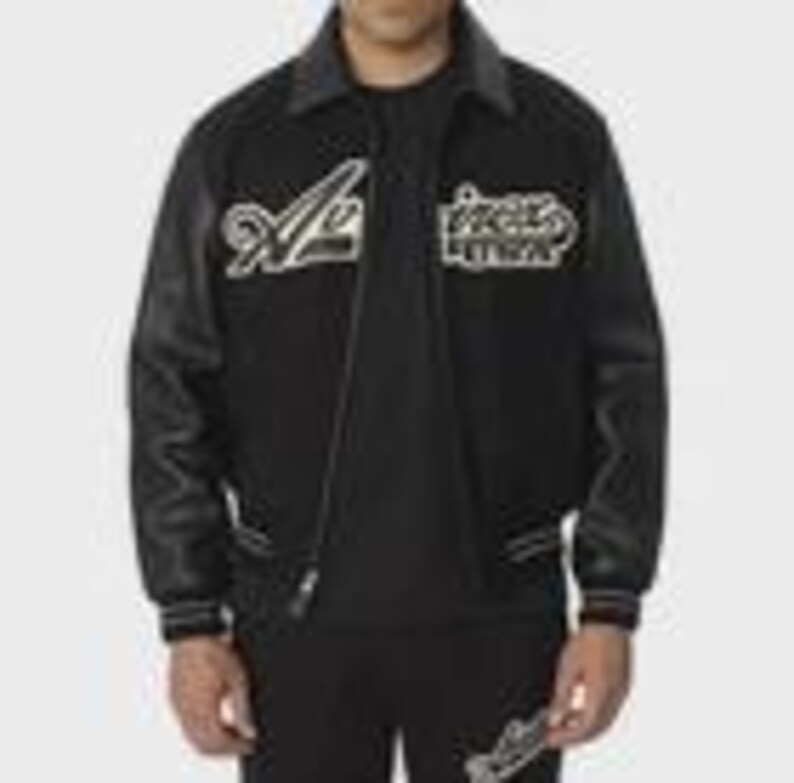 K&ouml;nnte beinhalten: Eine schwarze College-Jacke mit langen schwarzen &Auml;rmeln, einem spitzen Kragen und einem Frontrei&szlig;verschluss. Auf der Brust befindet sich der wei&szlig; gestickte Schriftzug Aeropostale. Die &Auml;rmelb&uuml;ndchen und der Saum sind mit schwarz-wei&szlig; gestreift.