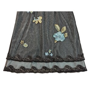 May include: A sheer, dark gray fabric with embroidered floral accents. The design features light blue and gold flowers, with a scalloped, embroidered border in black and gold. The fabric appears to be layered, creating depth and texture.