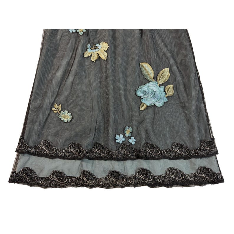 May include: A sheer, dark gray fabric with embroidered floral accents. The design features light blue and gold flowers, with a scalloped, embroidered border in black and gold. The fabric appears to be layered, creating depth and texture.