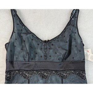 May include: A black and blue formal dress with a V-neckline and spaghetti straps. The dress features a satin waistband and a sheer overlay adorned with sequins and beaded details. The hemline is decorated with a floral lace design.