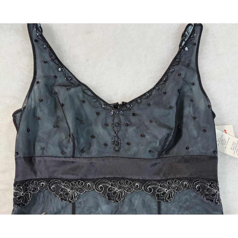May include: A black and blue formal dress with a V-neckline and spaghetti straps. The dress features a satin waistband and a sheer overlay adorned with sequins and beaded details. The hemline is decorated with a floral lace design.