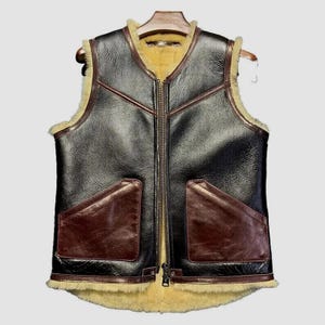 以下が含まれることがあります： 黒革のベスト。茶色のアクセントとフルレングスのジッパーが付いています。ベストには2つのフロントポケットとシアリングの裏地が付いています。木製のハンガーにかかっています。