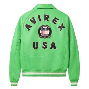 Puede incluir: Chaqueta de cuero verde brillante con la palabra "AVIREX" arqueada en la parte superior de la espalda y "USA" debajo de un parche circular con un dise&ntilde;o de bandera estadounidense. La chaqueta tiene cuello, pu&ntilde;os acanalados y dobladillo a rayas.