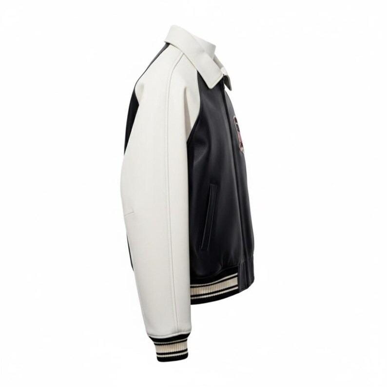 Puede incluir: Chaqueta universitaria negra y blanca con cuello y mangas blancas. La chaqueta tiene un cuerpo negro con un peque&ntilde;o emblema en el pecho. Los pu&ntilde;os y el dobladillo presentan detalles a rayas.