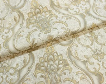 May include: Close-up of a roll of wallpaper featuring a classic damask pattern. The design includes scrolling vines and floral elements in shades of gold and cream, creating a textured, elegant look. The wallpaper has a subtle crackle effect.