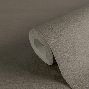 May include: A roll of textured wallpaper in a neutral taupe color. The paper has a woven appearance, with visible vertical and horizontal lines. The roll is partially unrolled, revealing the paper's thickness and texture. The wallpaper is suitable for interior design projects.