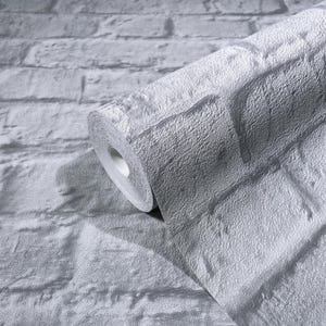 May include: A roll of textured, gray brick-patterned wallpaper. The wallpaper is unrolled, revealing the brick design. The color is a muted gray, with variations in tone to mimic the look of real bricks. The roll is partially unraveled.