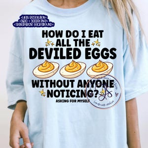 May include: Light blue t-shirt with the text "HOW DO I EAT ALL THE DEVILED EGGS WITHOUT ANYONE NOTICING?" and illustrations of deviled eggs. The shirt also has the text "ASKING FOR MYSELF" and a small logo.