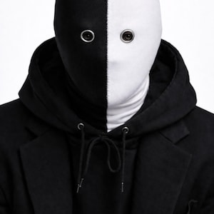May include: A full-head mask split vertically into black and white halves, featuring two circular eye openings with silver-toned metal grommets. The mask is worn with a black hooded sweatshirt layered under a black blazer with a notched lapel.