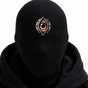 Puede incluir: Conjunto negro de sudadera con capucha y abrigo. Un broche decorativo en forma de ojo con iris naranja y marco metálico está fijado a la capucha. El atuendo es completamente negro, creando una apariencia misteriosa y llamativa.