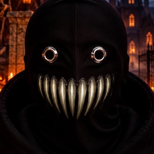 May include: A black hooded sweatshirt featuring a mask with metallic silver circular eye cutouts and a wide, jagged, metallic silver tooth grin. The text OTKYDACH is printed in white on the chest area, with a dripping font style.