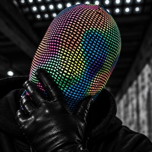 May include: A full-head balaclava featuring a vibrant, multi-colored grid pattern with a reflective finish. The head covering displays a spectrum of rainbow hues against a dark background, paired with black leather gloves and a black hooded sweatshirt.