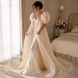 Elegant floor-length bridal robe with dramatic puff sleeves crafted from lightweight sheer fabric. Romantic wedding robe available in white and champagne, perfect for bridal getting ready photos, honeymoon, bridal boudoir, and luxury wedding morning styling.
