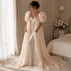 Elegant floor-length bridal robe with dramatic puff sleeves crafted from lightweight sheer fabric. Romantic wedding robe available in white and champagne, perfect for bridal getting ready photos, honeymoon, bridal boudoir, and luxury wedding morning styling.