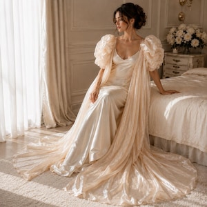 Elegant floor-length bridal robe with dramatic puff sleeves crafted from lightweight sheer fabric. Romantic wedding robe available in white and champagne, perfect for bridal getting ready photos, honeymoon, bridal boudoir, and luxury wedding morning styling.