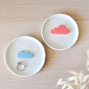 Op de afbeelding: Twee witte keramische schalen met een wolkontwerp. Een schaal heeft een blauwe wolk en een zilveren ring, de andere schaal heeft een roze wolk.