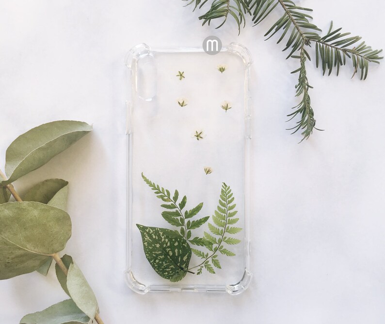 K&ouml;nnte beinhalten: Eine transparente Handyh&uuml;lle mit einem Design aus gepressten Blumen. Die H&uuml;lle zeigt kleine wei&szlig;e Bl&uuml;ten und gr&uuml;ne Farne.