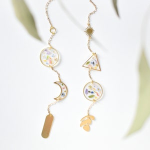 May include: A gold chain with a variety of charms, including a crescent moon, a circle, a triangle, a leaf, and a rectangle. Each charm is filled with pressed flowers in shades of pink, blue, and yellow.