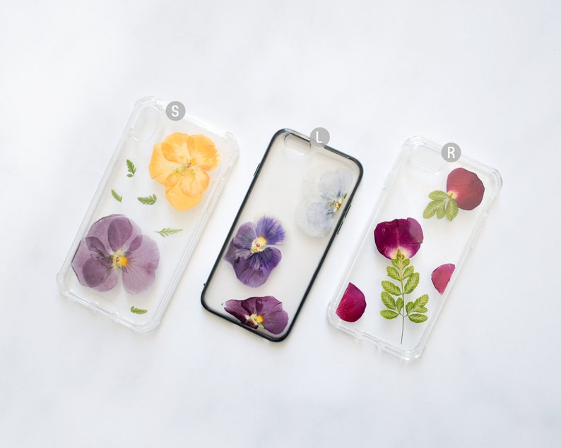 K&ouml;nnte beinhalten: Drei transparente Handyh&uuml;llen mit gepressten Blumen darin. Die H&uuml;llen sind transparent und zeigen die Blumen im Detail. Die Blumen sind lila, gelb und rot.