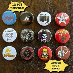 Puede incluir: Un conjunto de doce insignias redondas con logotipos de bandas y texto, incluyendo "ADOLESCENTS", "BLACK FLAG" y "THE CLASH". Las insignias son de varios colores, incluyendo azul, negro, blanco y rojo. El texto "CHOOSE YOUR PACK!" también es visible.