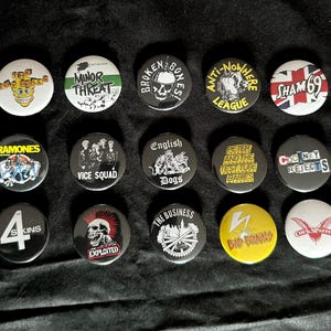 Könnte beinhalten: Eine Sammlung von fünfzehn runden Ansteckbuttons mit verschiedenen Logos und Grafiken von Punk-Rock-Bands, darunter The Toy Dolls, Minor Threat, Broken Bones, Anti-Nowhere League, Sham 69, Ramones, Vice Squad, English Dogs, Peter and the Test Tube Babies, Cockney Rejects, The 4-Skins, The Exploited, The Business, Bad Brains und Cock Sparrer.