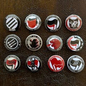 Puede incluir: Una colección de doce chapas redondas con diversos gráficos políticos y sociales. Los diseños incluyen el símbolo de las tres flechas, un gato, una rana, un dinosaurio, el número 666 en una bandera y textos como Antifascist Action.