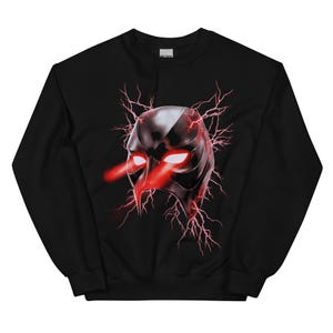 May include: A black long-sleeve sweatshirt featuring a central graphic of a dark, metallic-looking mask. The mask has glowing red eyes emitting beams of light, surrounded by jagged red lightning bolts that extend outward across the chest area.
