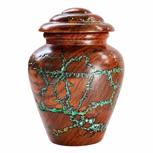 May include: A polished brown wooden urn with a rounded lid and a wide body. The surface features intricate, branching cracks filled with a vibrant, textured turquoise-green inlay that creates a striking contrast against the dark wood grain.