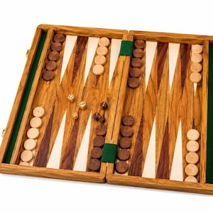 May include: A wooden backgammon board featuring a natural wood grain finish with alternating dark and light wood triangular points. The board includes dark and light wooden checkers arranged in stacks, along with two pairs of dice.
