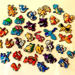 Könnte beinhalten: Eine Sammlung pixeliger Pokémon-Charaktere in verschiedenen Farben, darunter Orange, Blau, Grün und Lila. Die Figuren sind auf einer weißen Oberfläche angeordnet und zeigen eine Vielzahl beliebter Kreaturen aus dem Franchise.