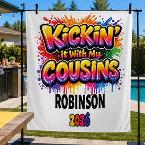 May include: A white rectangular backdrop banner featuring a colorful graffiti-style design with the text Kickin' it With My COUSINS, the name ROBINSON, and the year 2026. The banner is mounted on a black metal stand, displaying vibrant paint splatters.