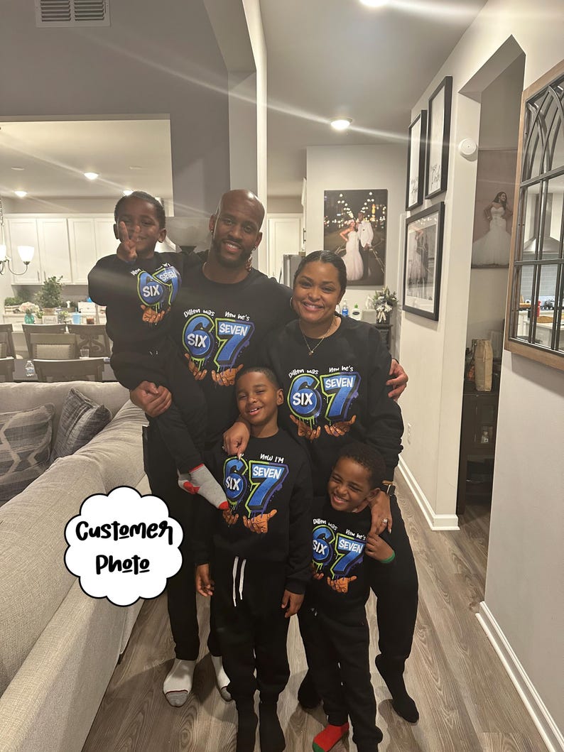 May include: A family of six wearing matching black sweatshirts and sweatpants. The sweatshirts have a blue and green graphic that says "Dillon was SIX, Now he's SEVEN". The family is smiling and posing for a photo.