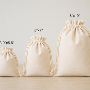 May include: Three beige drawstring bags of varying sizes: 3.9"x5.5", 5"x7", and 8"x10". Each bag features a gathered top and a natural-colored drawstring closure. The bags are made of a soft, neutral-toned fabric.