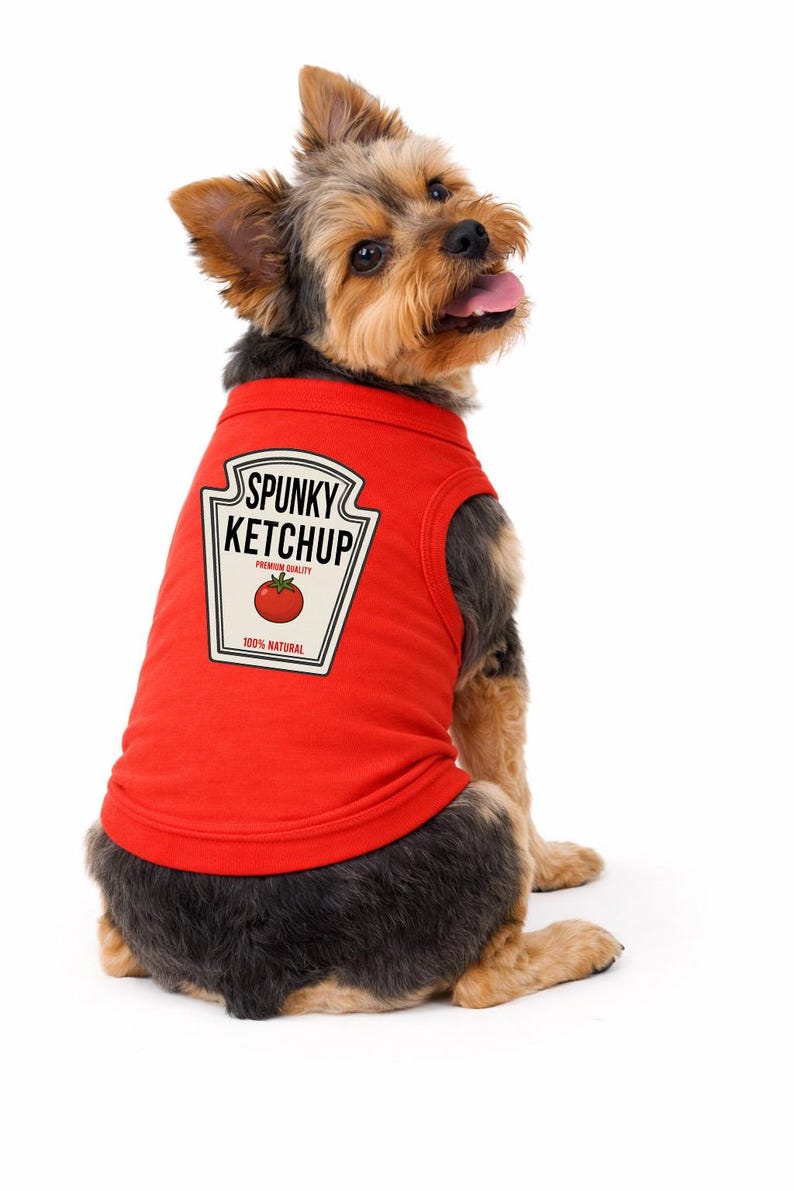 May include: A red sleeveless pet shirt featuring a graphic print of a ketchup bottle label with the text SPUNKY KETCHUP, PREMIUM QUALITY, and 100% NATURAL, along with a red tomato illustration, worn by a small brown and black Yorkshire Terrier dog.