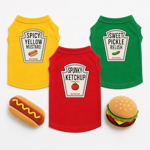 May include: Three sleeveless shirts in yellow, red, and green, each featuring a condiment bottle label graphic. The yellow shirt reads SPICY YELLOW MUSTARD, the red reads SPUNKY KETCHUP, and the green reads SWEET PICKLE RELISH. Includes plush hot dog and burger toys.