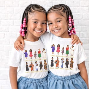 May include: Two young girls wearing white t-shirts featuring a colorful illustration of various women in different professions. The illustration includes figures in dresses, uniforms, and professional attire. The girls are smiling and embracing each other.
