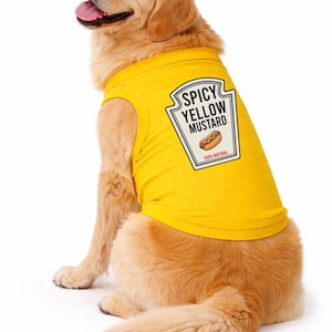 May include: A golden retriever wearing a bright yellow sleeveless pet shirt. The back of the shirt features a white label graphic with a black border, black text reading SPICY YELLOW MUSTARD, a hot dog illustration, and the text 100% NATURAL.