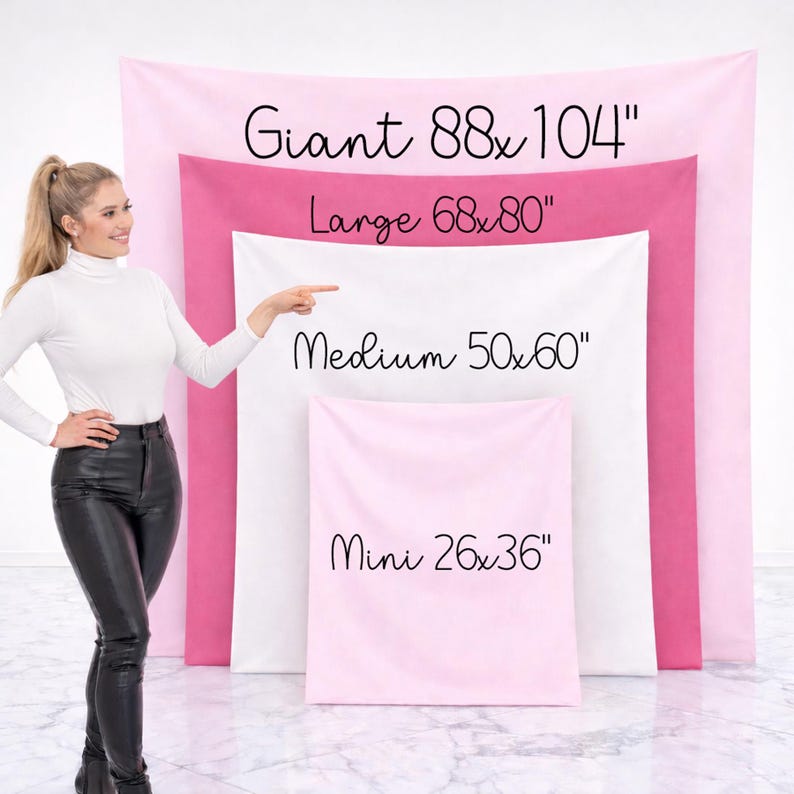 May include: A woman points to a display of pink and white tapestries of varying sizes. The largest tapestry is 88 x 104 inches, followed by 68 x 80 inches, 50 x 60 inches, and the smallest at 26 x 36 inches. The text on the tapestries indicates their sizes.