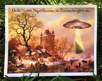May include: A Christmas card with a winter landscape scene. The card features a UFO beaming a Christmas tree. Text reads, "On the Twelfth Day of Christmas, the Martians brought to me..."