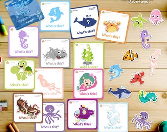 Peut inclure: Un jeu éducatif pour enfants avec des cartes colorées représentant des créatures marines et la question "Qu'est-ce que c'est ?" ainsi que des autocollants assortis. Le jeu est conçu pour apprendre de nouveaux mots et jouer à associer.