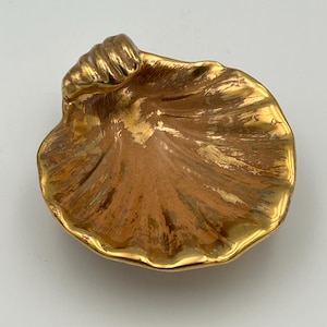 May include: A gold-colored, seashell-shaped dish with a textured surface. The dish has a glossy finish and is likely made of ceramic or metal. The dish is a decorative item.