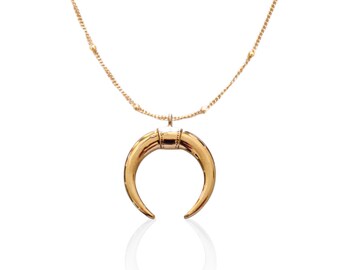May include: A gold necklace with a crescent moon pendant. The chain is made of small gold beads.