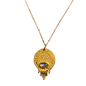 May include: A gold necklace with a round pendant featuring a lotus flower design and a clear gemstone. The pendant is accented with smaller gemstones.
