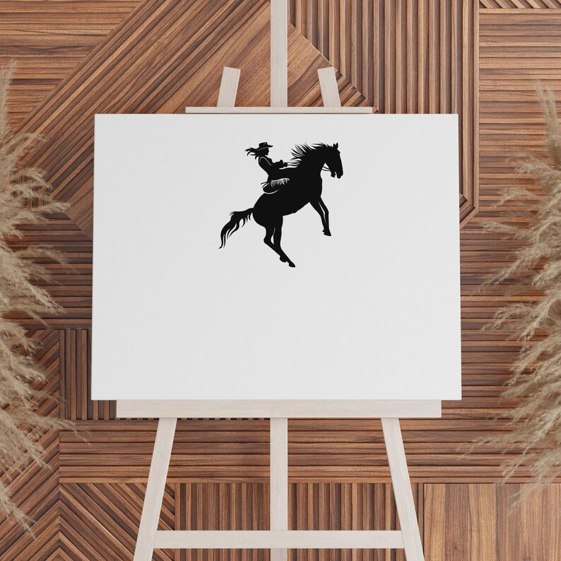 May include: A black silhouette of a person riding a rearing horse, set against a white canvas. The rider wears a hat and is seated on the horse. The image is displayed on a wooden easel, with a textured wooden background.