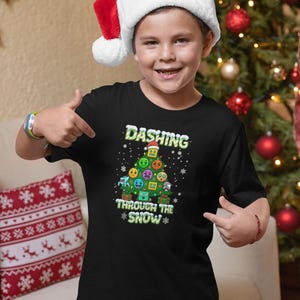 May include: A black t-shirt with the text "Dashing Through The Snow" and a Christmas tree design made of emoji faces. The person in the image is wearing a red and white Santa hat.