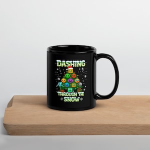 Könnte beinhalten: Schwarze Keramik-Tasse mit einem Weihnachtsbaum-Design aus bunten geometrischen Formen und dem Text "Dashing Through The Snow". Die Tasse hat einen großen Henkel und steht auf einer Holzoberfläche.