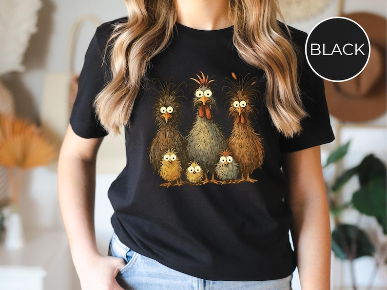 May include: Black t-shirt featuring a whimsical illustration of a chicken family. The design includes a rooster, hens, and chicks with expressive eyes and detailed feathering. A fun and unique graphic tee.